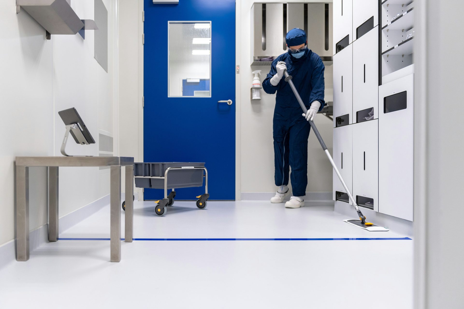 A person in protective blue coveralls mopping a white floor in a sterile room